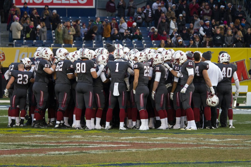 The football team huddles up at midfi eld during the Lehigh rivalry game at Yankee Stadium on Nov. 22, 2014. Ross Scheuerman, number 29, is pictured in the middle of the huddle. [Photo Courtesy of Hana Isihara ‘17]